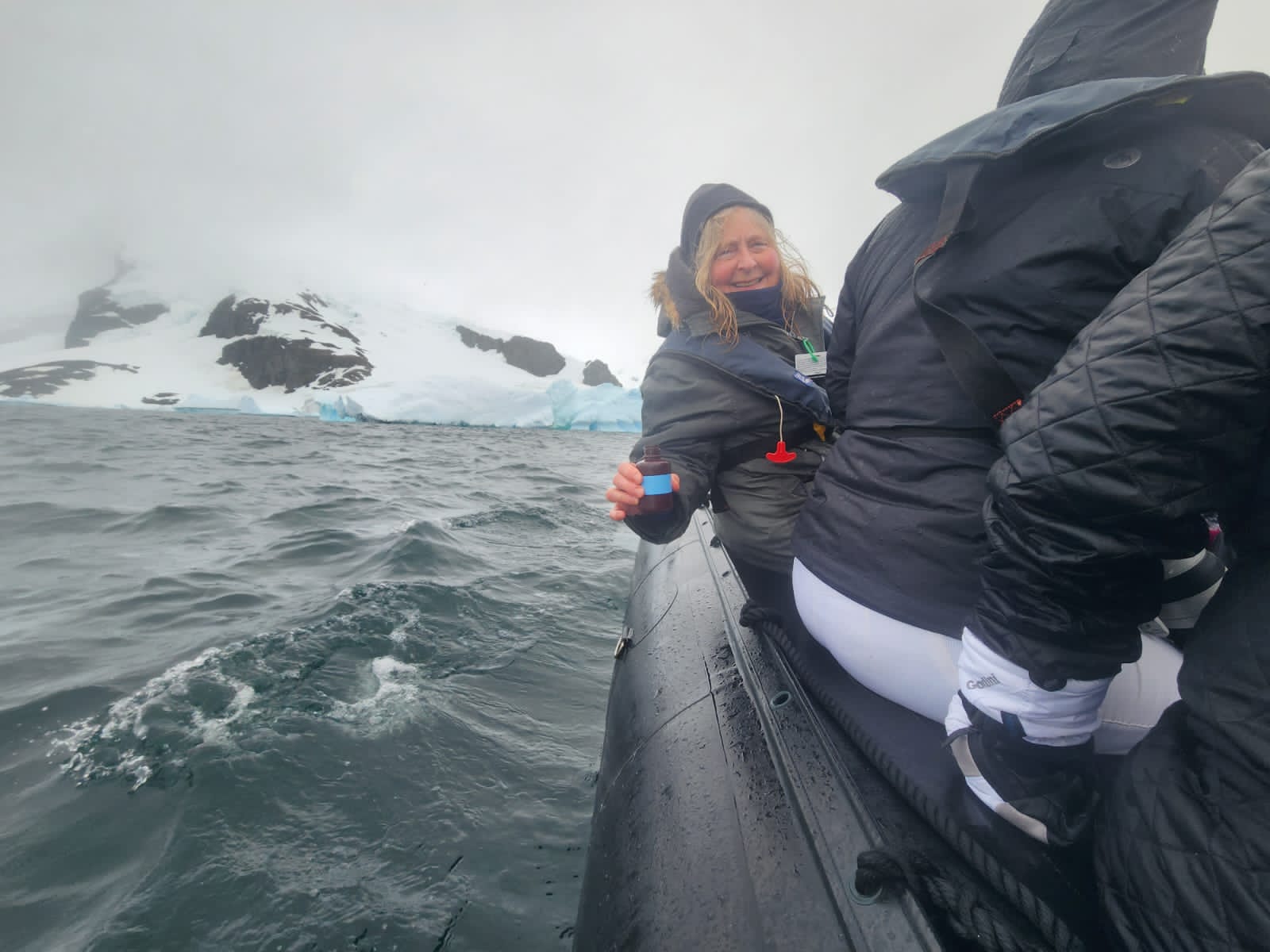 Traveler on a Zodiac in Antarctic waters holding a plankton sample bottle with icebergs behind