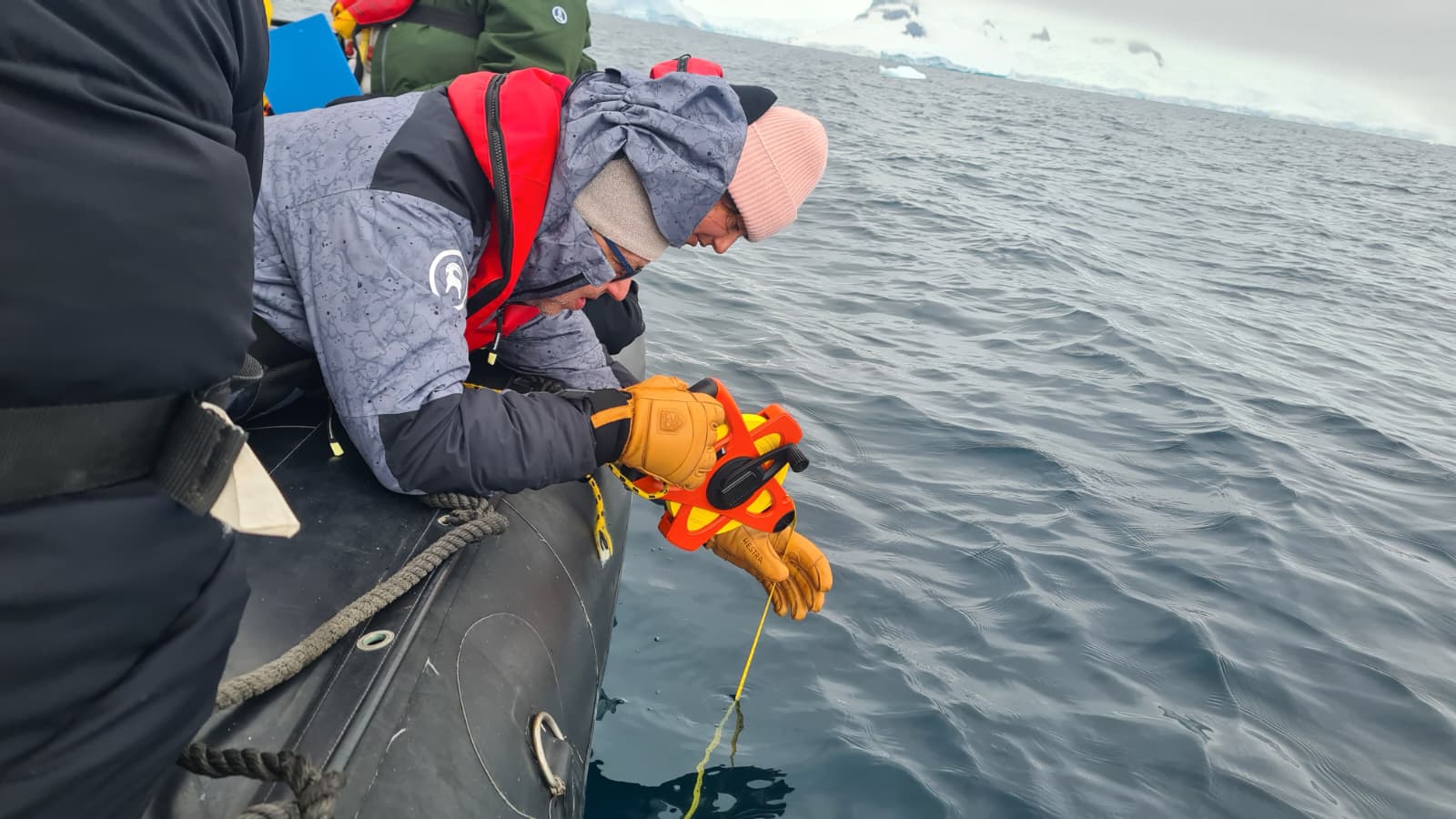 Scientist deploying a yellow water-sampling line over the side of a Zodiac in calm polar water