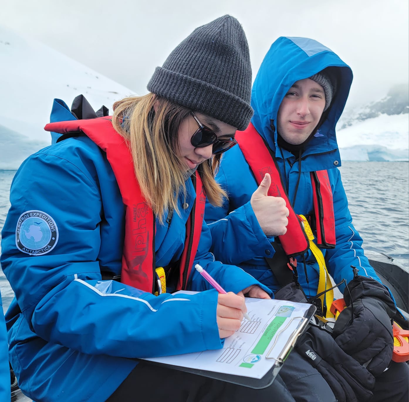 Two travelers in expedition gear recording observations on a FjordPhyto datasheet aboard a Zodiac