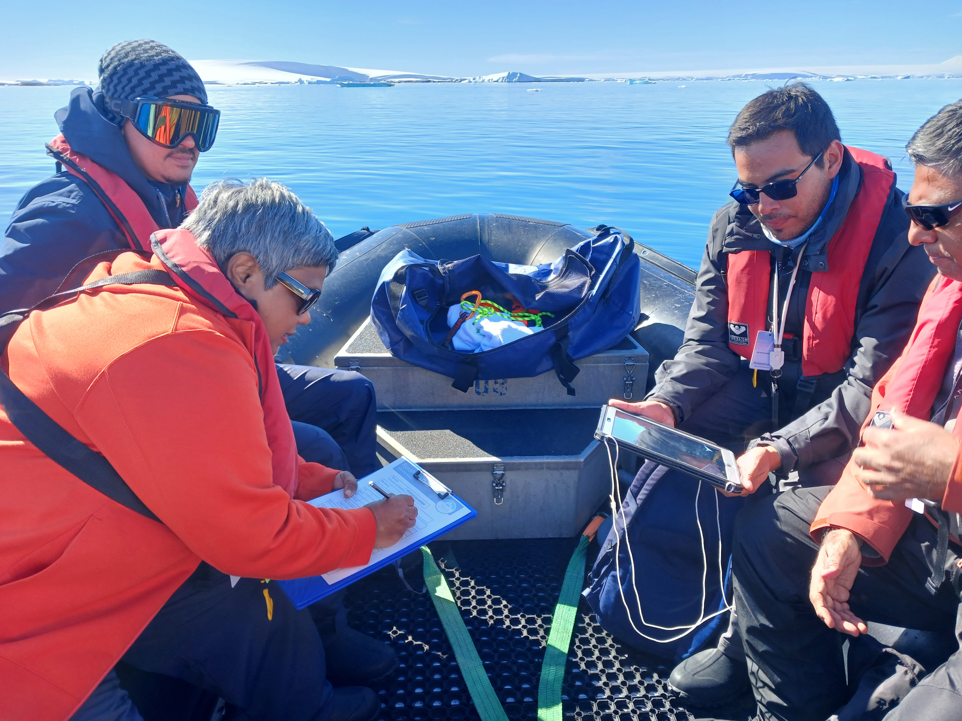 Expedition team on a Zodiac in calm Antarctic waters recording observations on a datasheet while reviewing a tablet