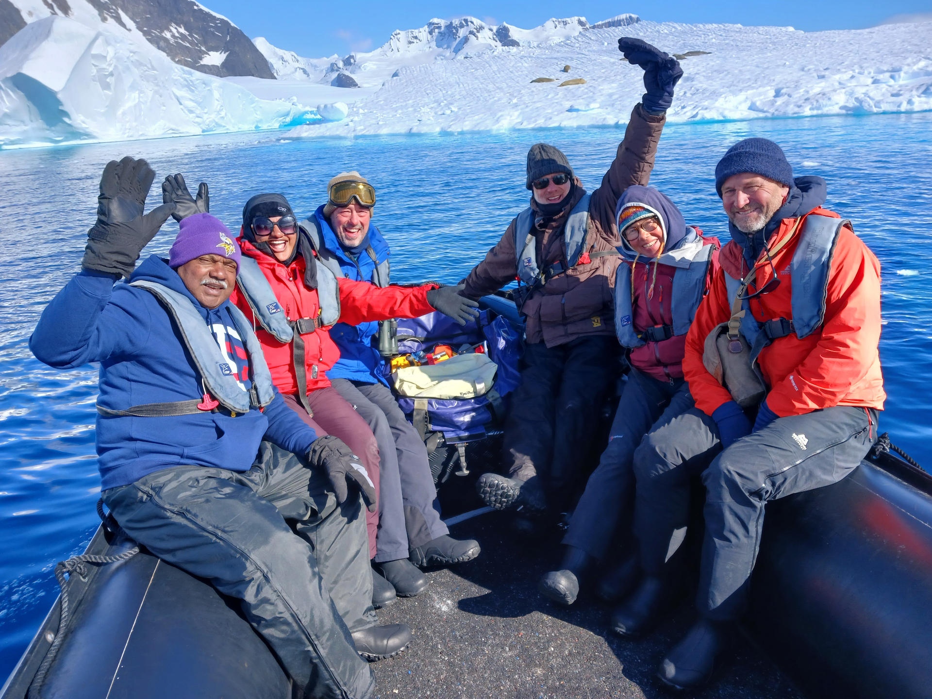 Group of expedition travelers smiling aboard a Zodiac with bright Antarctic ice behind them