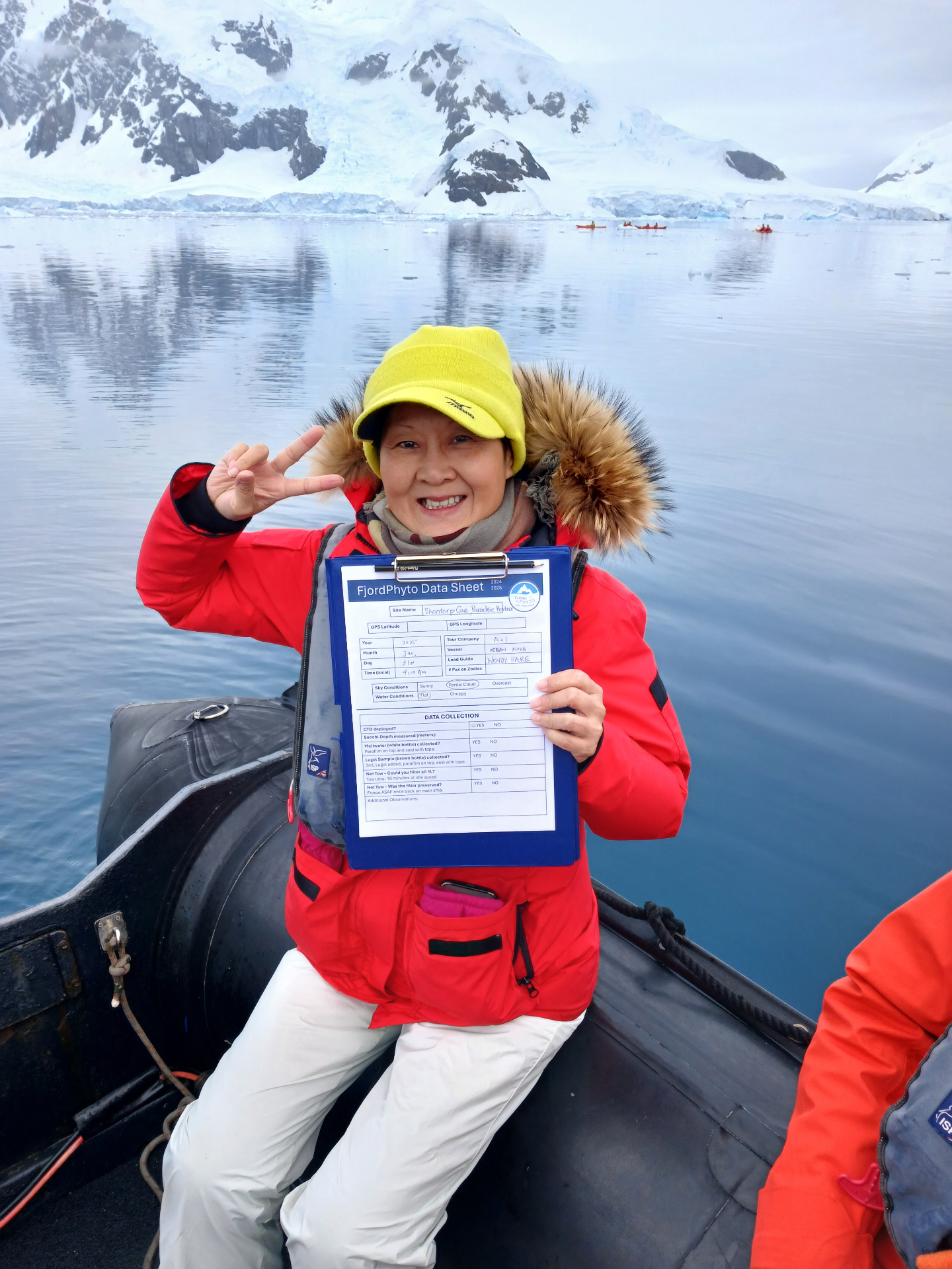 Traveler in a red parka holding a completed FjordPhyto data sheet on a Zodiac in Antarctica