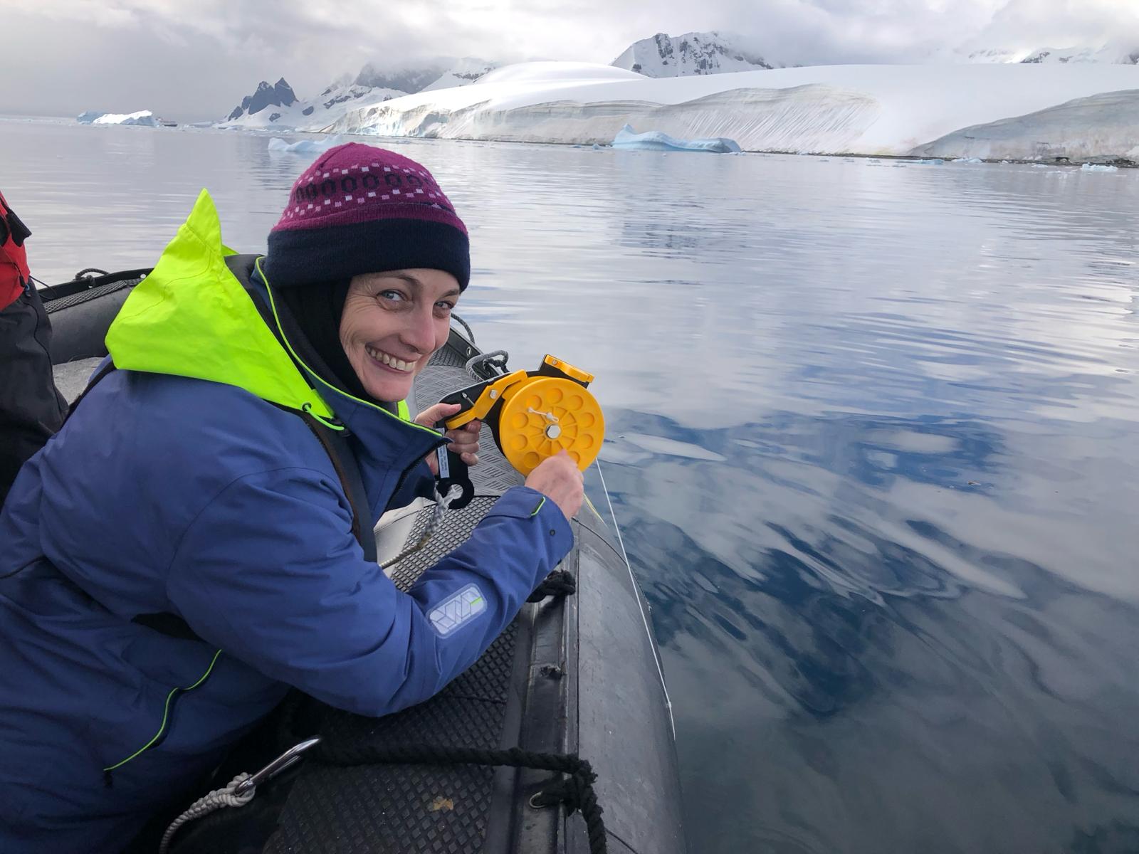 Traveler smiling while operating a yellow water-sampling reel from a Zodiac in calm Antarctic water