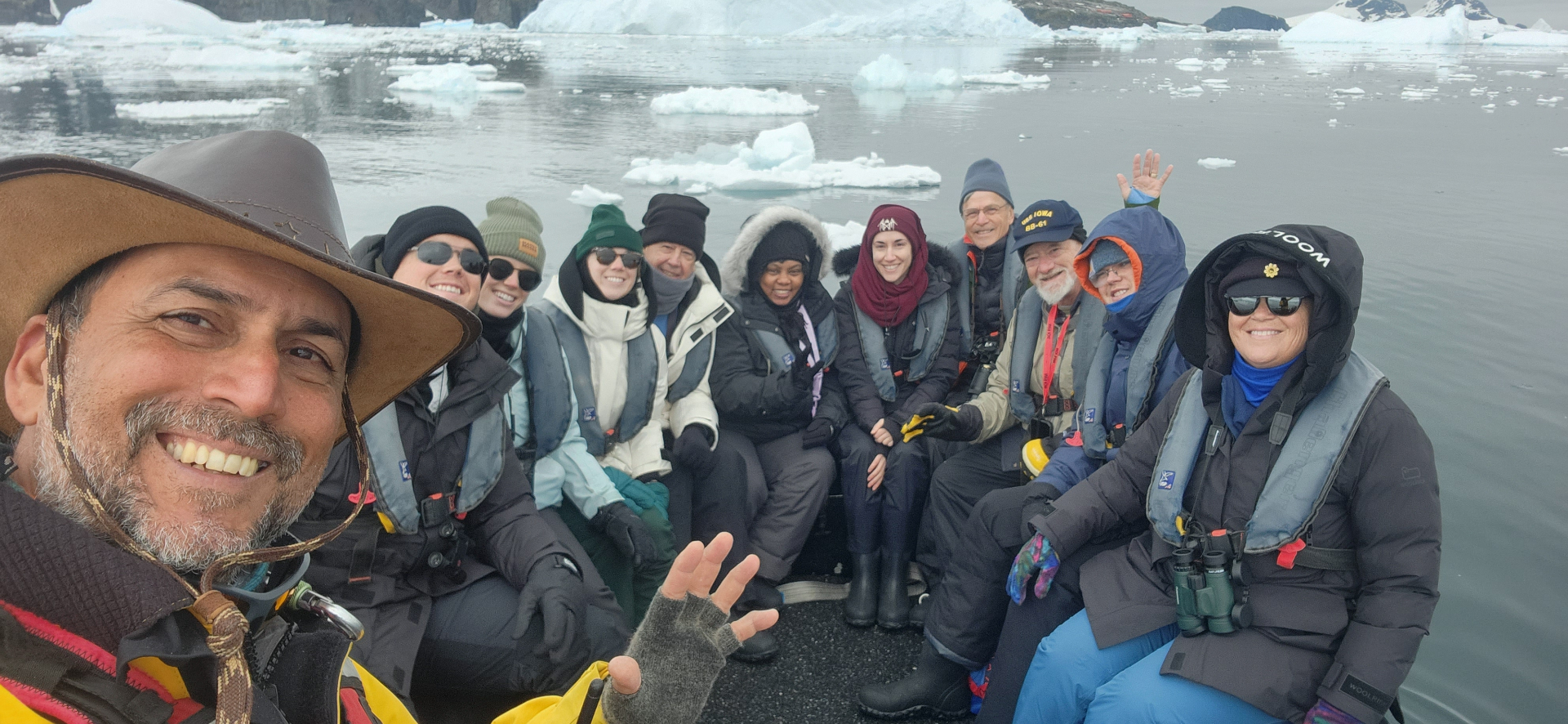 Large group selfie from a Zodiac excursion with bundled travelers and Antarctic ice in the background